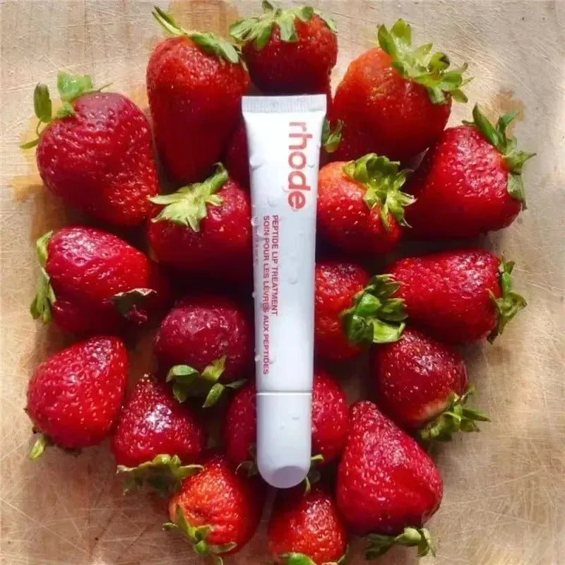 Tube of 'rhode' cream surrounded by strawberries on a wooden surface