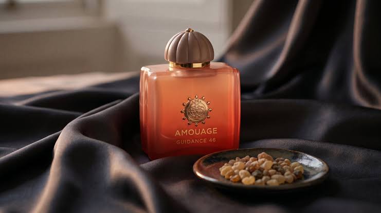Amouage perfume bottle on dark fabric with a small dish of nuts.