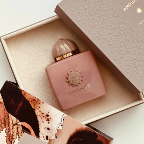 Pink Amouage perfume bottle in an open box with a patterned fabric background