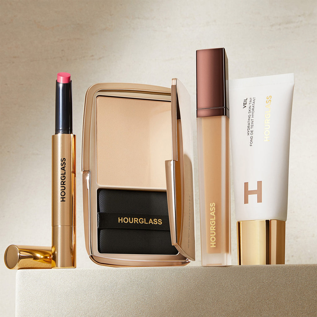 Hourglass makeup products including a lipstick, compact mirror, and foundation on a beige background
