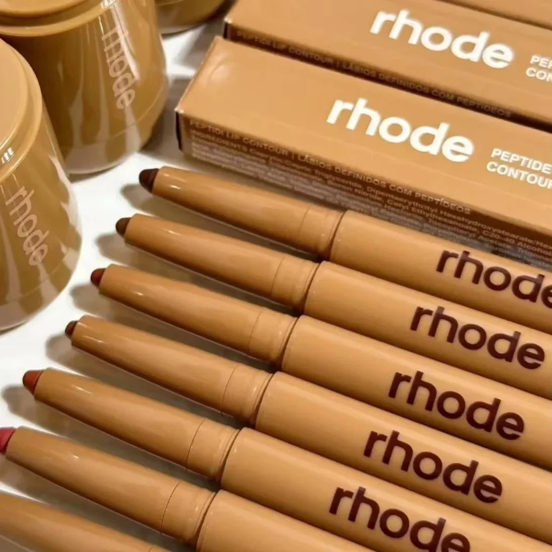 Row of Rhode cosmetic pencils with packaging on a white surface