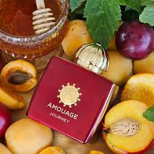 Amouage Journey perfume bottle in deep red with a gold cap, surrounded by fresh apricots, a honey pot, and green leaves.
