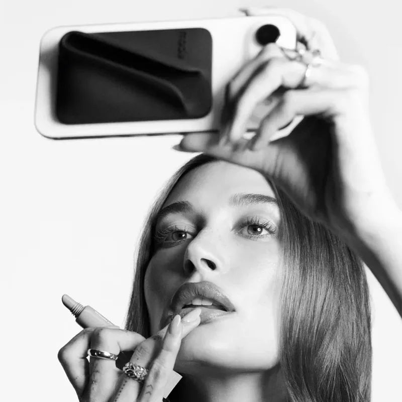 Black and white image of a woman holding a smartphone with a makeup mirror app open.