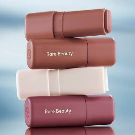 Stack of 'Rare Beauty' lip products on a gradient background