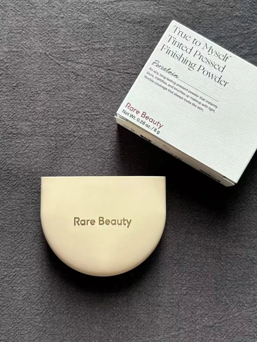 Rare Beauty pressed powder and packaging on a dark surface