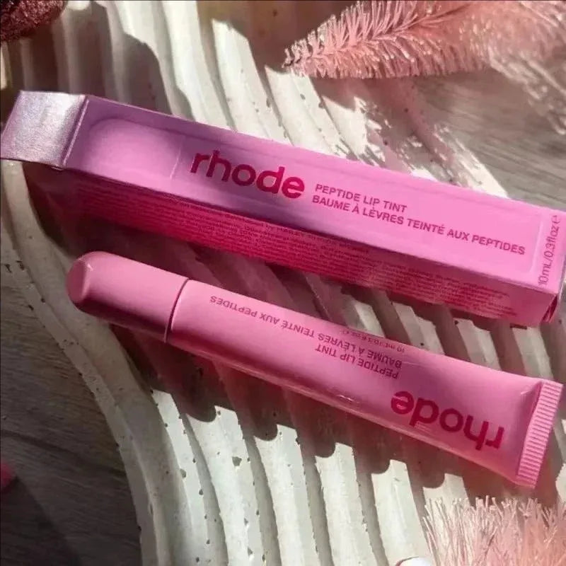 Pink lip tint with 'rhode' branding on a textured surface