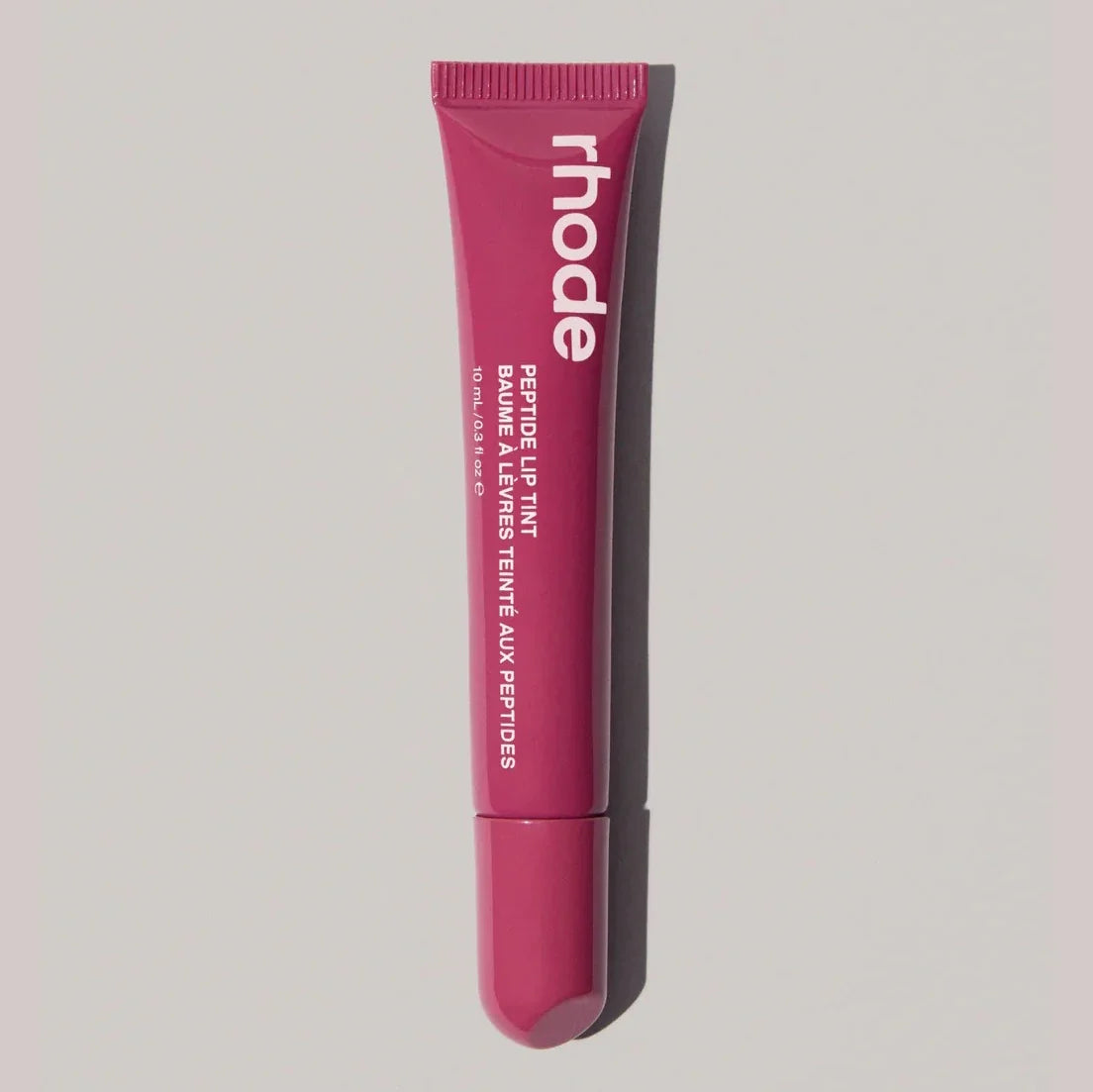 Pink lip balm tube with 'rhode' branding on a light gray background