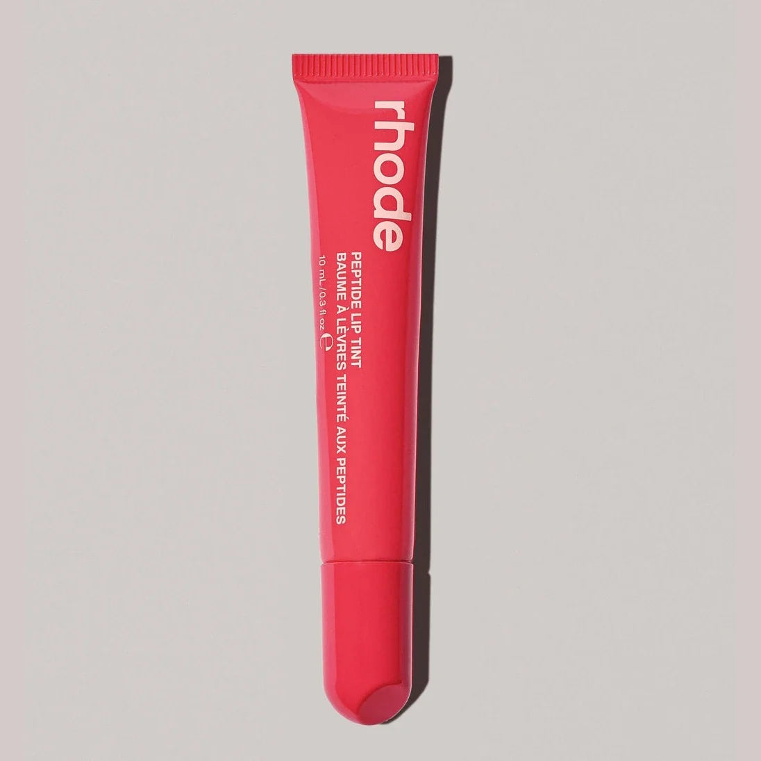 Red lip balm tube with 'rhode' branding on a gray background